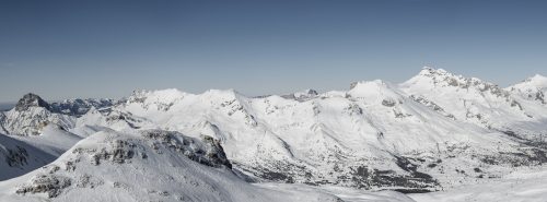 This panoramic photo captures the majestic peaks of the Devoluy mountains blanketed in freshly fallen snow, basked in the warm glow of the bright sun.